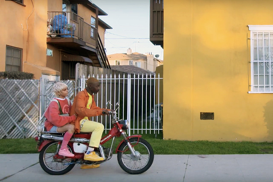 A photo still of the main couple sitting on a motorcycle, driving down the street, in the short film Know the Ledge by Ibra Ake.