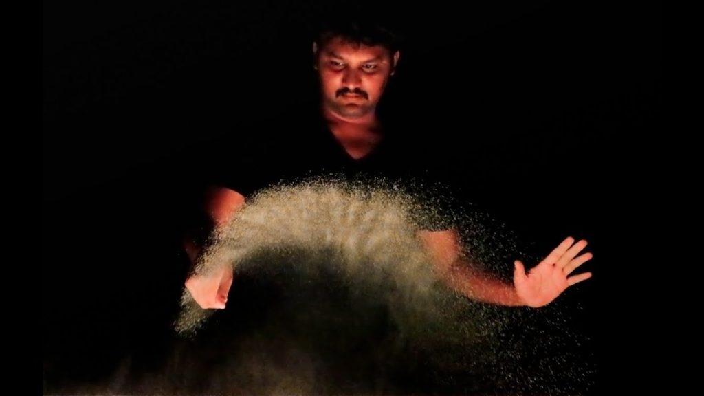 A photo of artist Nitish Bharti throwing sand into the air.
