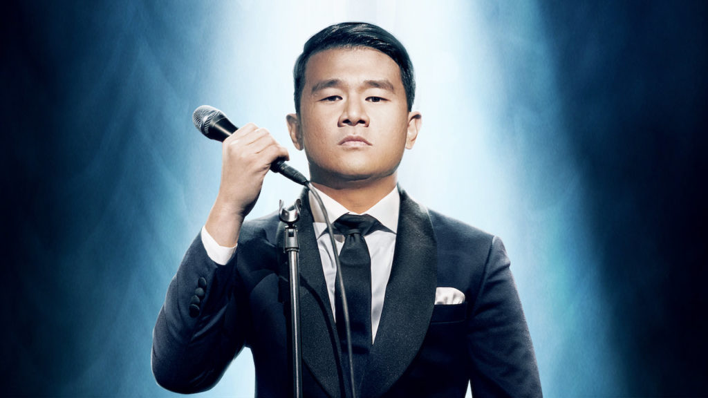 A promotional photo of Ronny Chieng looking straight into the camera and holding a mic.