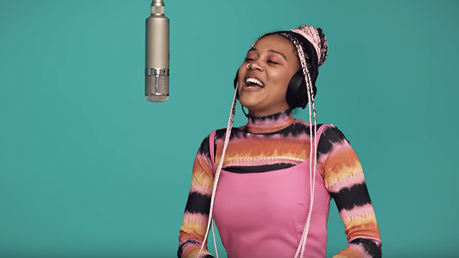 A photo still of singer Sho Madjozi singing into a mic from the video for John Cena.