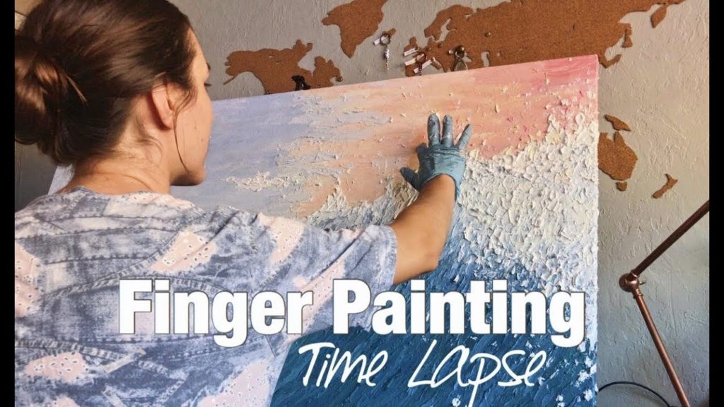 A photo of Dzvenyslava Valaga in front of her canvas in the process of creating a painting of ocean waves with her fingers.