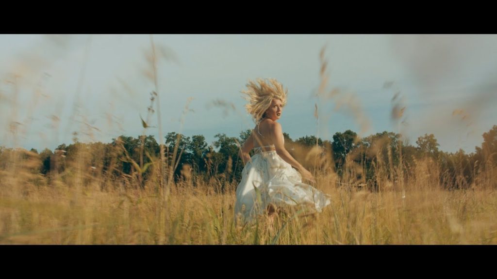 A photo still from the music video Foxes of Madison Malone running from the camera through a field.