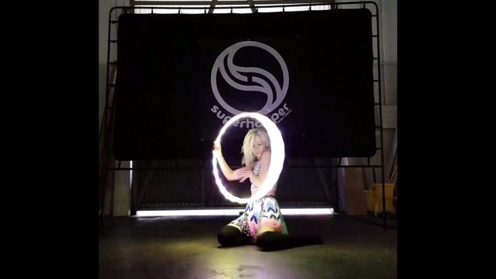 A photo of dancer Morgan Dancer with a hula hoop illuminated by LED lights framing her head.