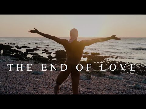 A photo of a dancer looking out at the ocean, arms outspread, with the sun setting on the horizon from the video The End of Love by Yanis Marshall.