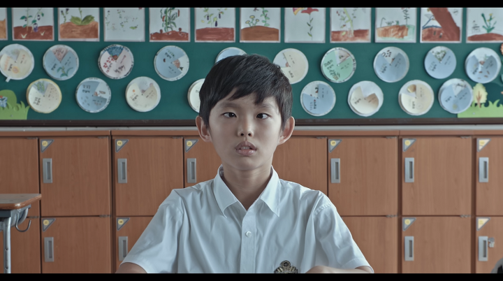 A photo still of the main character, Yuwol, staring cross eyed into the camera from the film The Boy Who Made the World Dance.