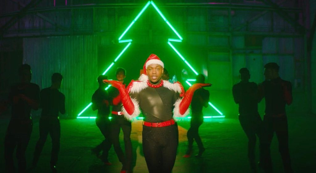 A photo of Todrick Hall from the music video of Bells, Bows, Gifts, Trees. A neon green outline of a Christmas tree is behind him.