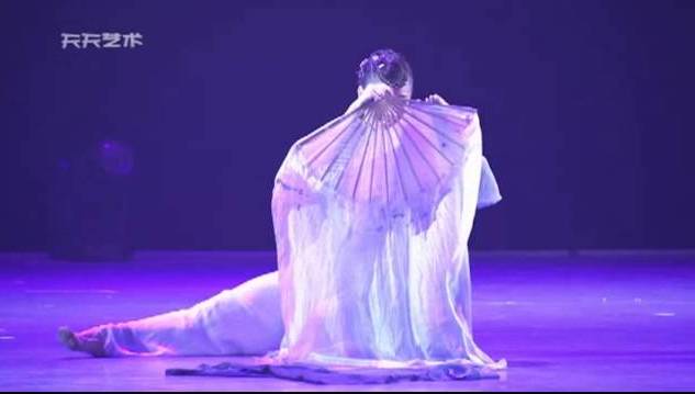 A photo of dancer Bi Ying mid-performance, holding her fan in front of her face.