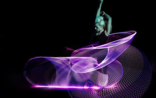A photo of Lisa Lottie mid-performance. The six hula hoops are just streaks of light, as they are moving so fast.