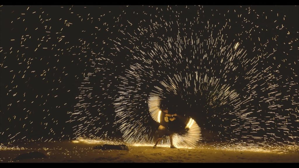 An image of a Poi Fire Dancer with sparks flying in circles around him.