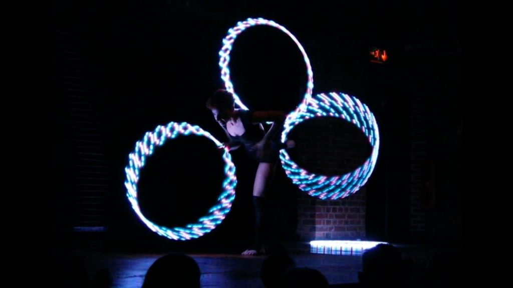 A photo of dancer Silvia Pavone mid-performance juggling three LED hula hoops.