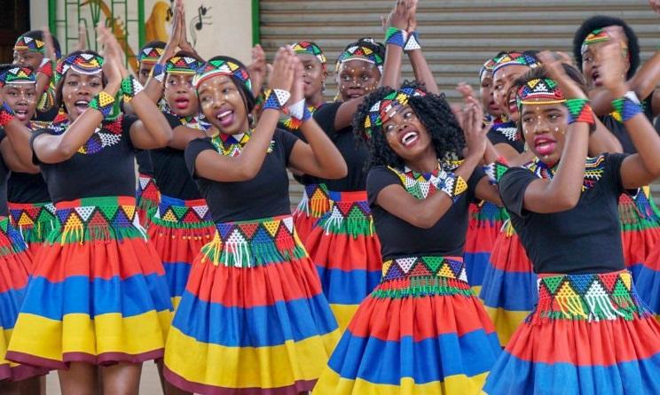A photo of members of the Ndlovu Youth Choir, all smiling and brightly dressed.
