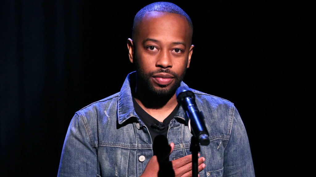 A photo of poet Rudy Francisco, standing in front of a mic, looking directly into the camera.