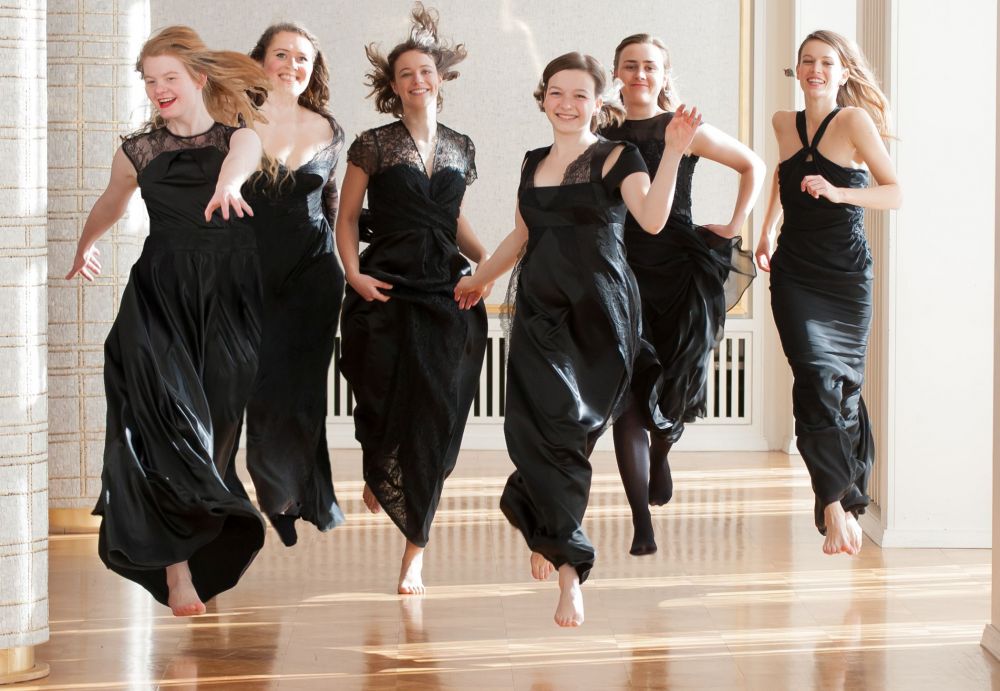A promotional photo of the six members of Sjaella, mid-jump as they run towards the camera.