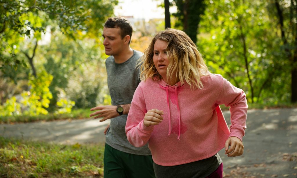 A photo still from Brittany Runs a Marathon, showing two characters running through a park, each of them looking deeply unhappy about it.