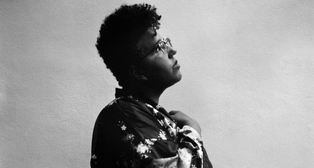 A photo of musician Brittany Howard in side profile, hand on her chest, looking up.
