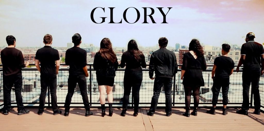A photo of nine members of Musicality, standing along a railing, backs to the camera, looking out over a cityscape.