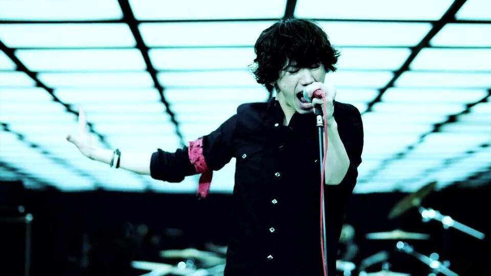 A photo still from the music video for Clock Strikes from One OK Rock, showing lead singer Takahiro Moriuchi singing aggressively into a mic.