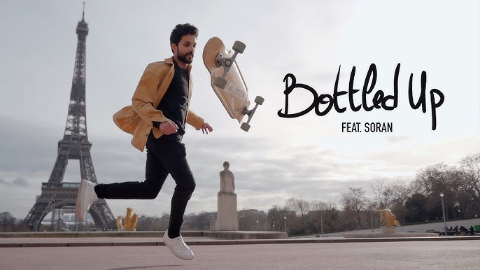 A photo of Lotfi Lamaali, mid-performance, with a longboard flipping through the air in front of him, and the Eiffel Tower in the background.