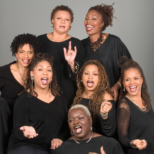 A promotional photo of the members of Sweet Honey in the Rock. They are all wearing black and are looking directly into the camera. Some of them look to be mid-song.