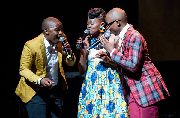 A photo of the three singers of the band The Soil, onstage, all three holding mics, mid-performance.