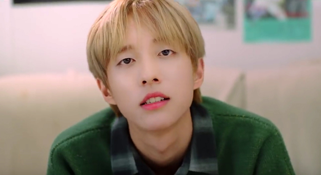 A close up photo of K-pop singer Holland sitting on a couch, staring straight into the camera.