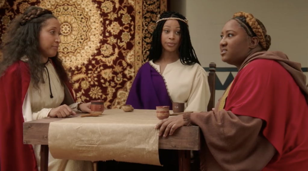 A photo still from The Last Supp-her, a sketch from A Black Lady Sketch Show, showing three female Black disciples sitting around a table gossiping with each other.