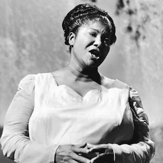 A black and white photo of Mahalia Jackson, mid-performance, singing on stage.