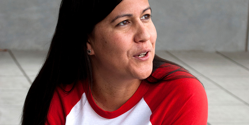 A close up photo of poet Natalie Diaz in a red and white shirt, looking off to the side to the right of the camera.