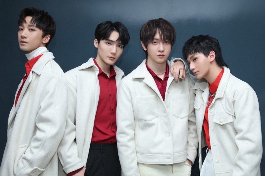 A promotional photo of TUBS. All four members are wearing white and red outfits and posing while looking straight into the camera.