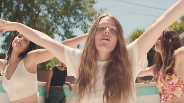 A photo still from the music video of Give a Little by Maggie Rogers. Three women are dancing in the sun with their arms in the air.