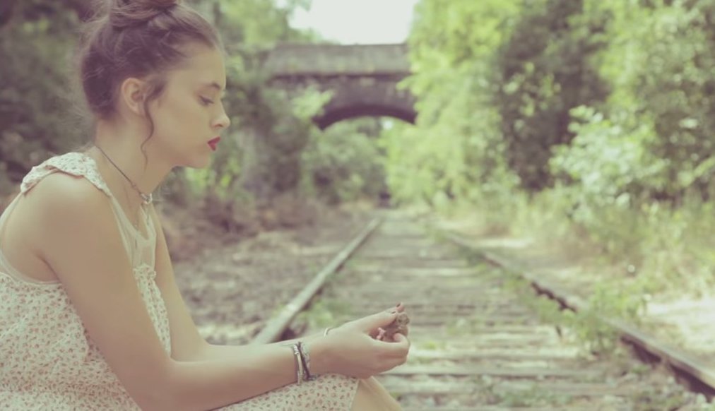 A photo still from the music video of Sans Toi by Pomme. She is sitting on a train track looking down at her hands.