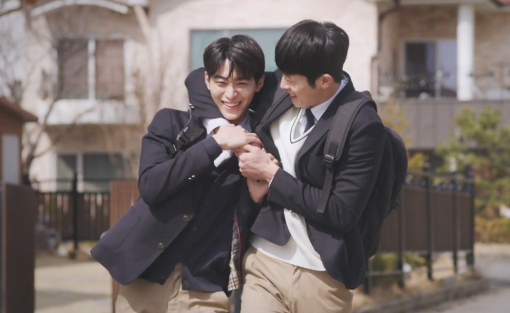 A photo still from Where Your Eyes Linger. Lead actors Han Gi-chan and Jang Eui-soo are wearing school uniforms, walking side by side, smiling widely with one having his arm around the other's neck.