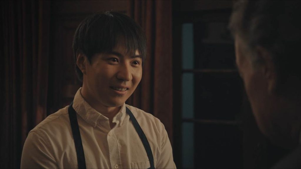 A photo still from the short film Dinner is Served. The photo is a close up of lead actor Qi Sun smiling at another character just out of frame.