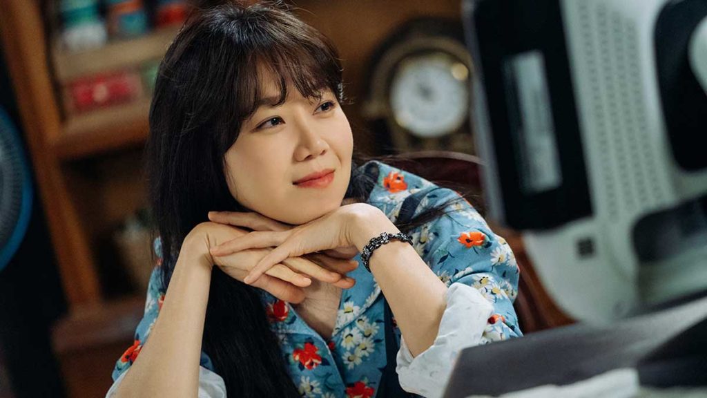 A photo still from When the Camellia Blooms. Lead actress Gong Hyo-jin is sitting at a table, head in her hands, smiling as she looks off to the right.