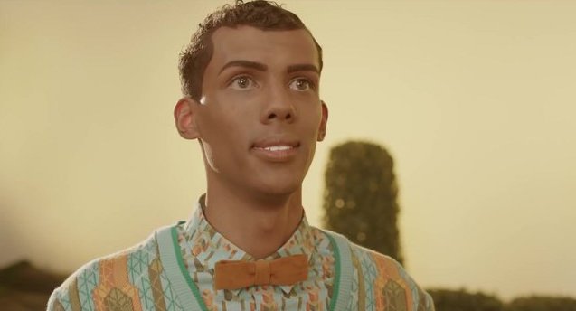 A photo still from the music video of Papaoutai by Stromae. The photo is a close up of Stromae posing like a mannequin and looking off into the distance.