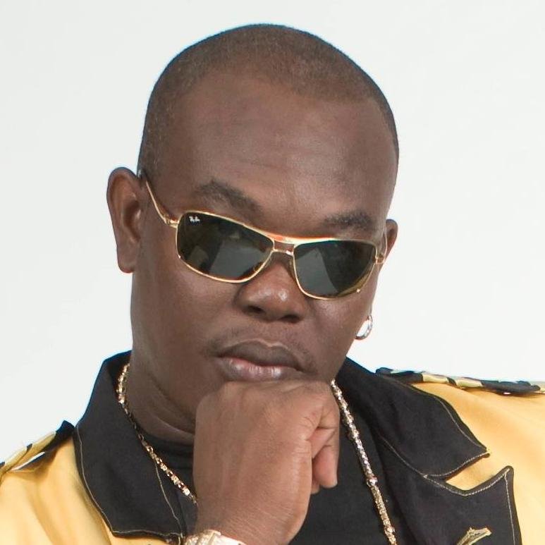 A close up photo of musician Supa G. He is resting his chin on his closed fist and staring straight into the camera through a pair of sunglasses.