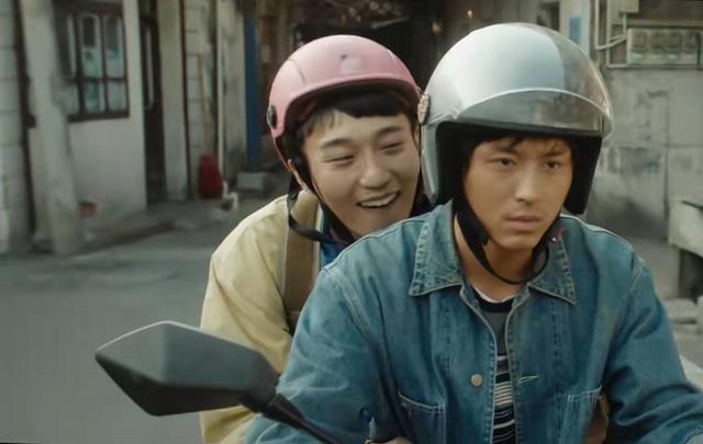 A photo still from the short film Brother by Zhao Wei. It shows lead actors Zhang Zhehan and Sen Wang. They are riding a motorcycle, one behind the other, both wearing helmets. The one in back is smiling while the one in front is not.