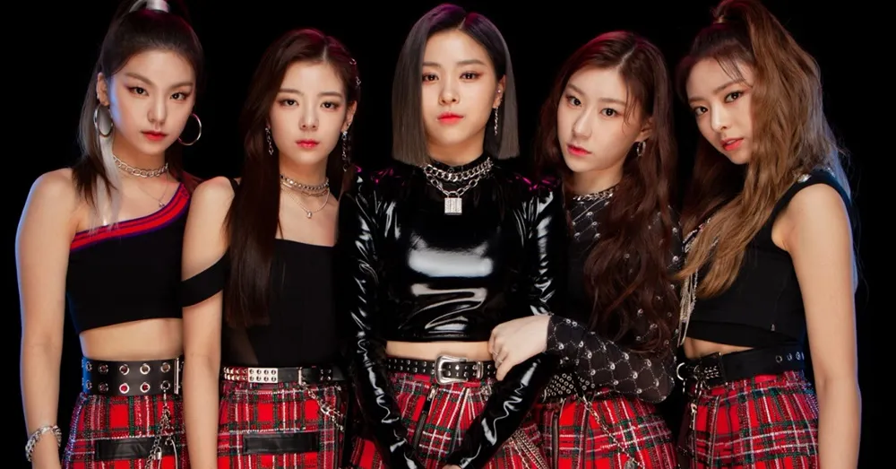 A promotional photo of Itzy. All five members are standing in a line, dressed in black and red, staring straight into the camera.
