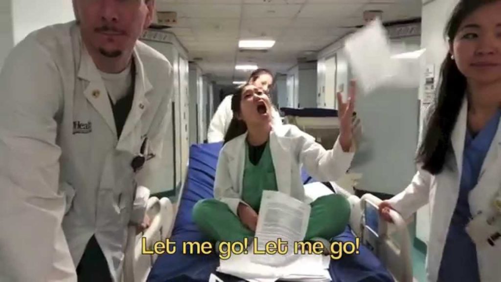 A photo from the video parody I Don't Know. A doctor in a white jacket is sitting on a gurney singing while other doctors wheel her through the hallways of a hospital.