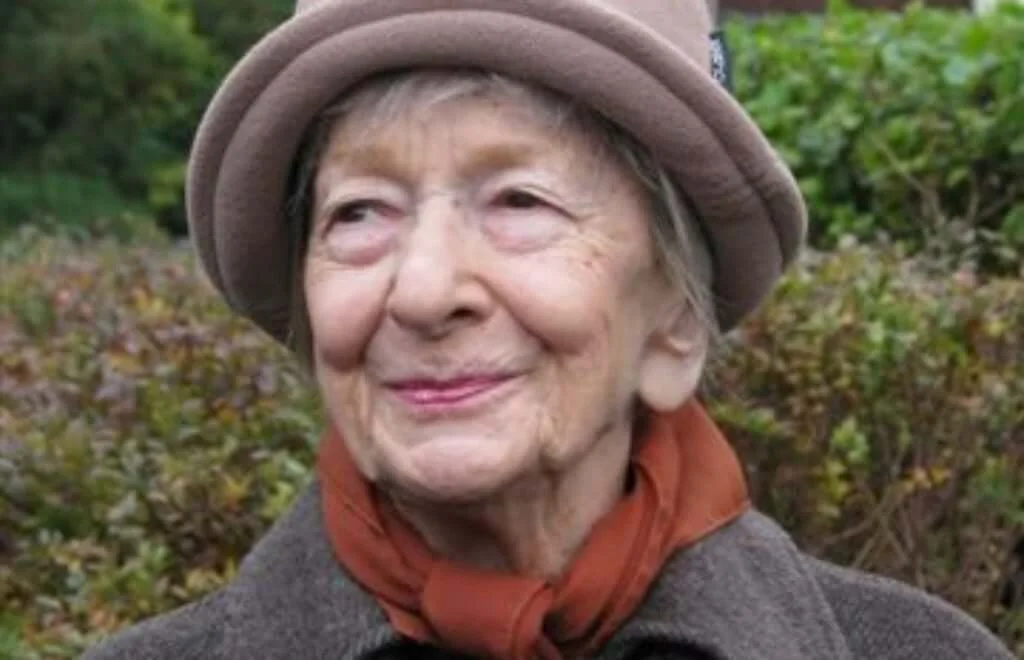 A close up photo of poet Wislawa Szymborska. She is smiling slightly and looking off camera to the left.