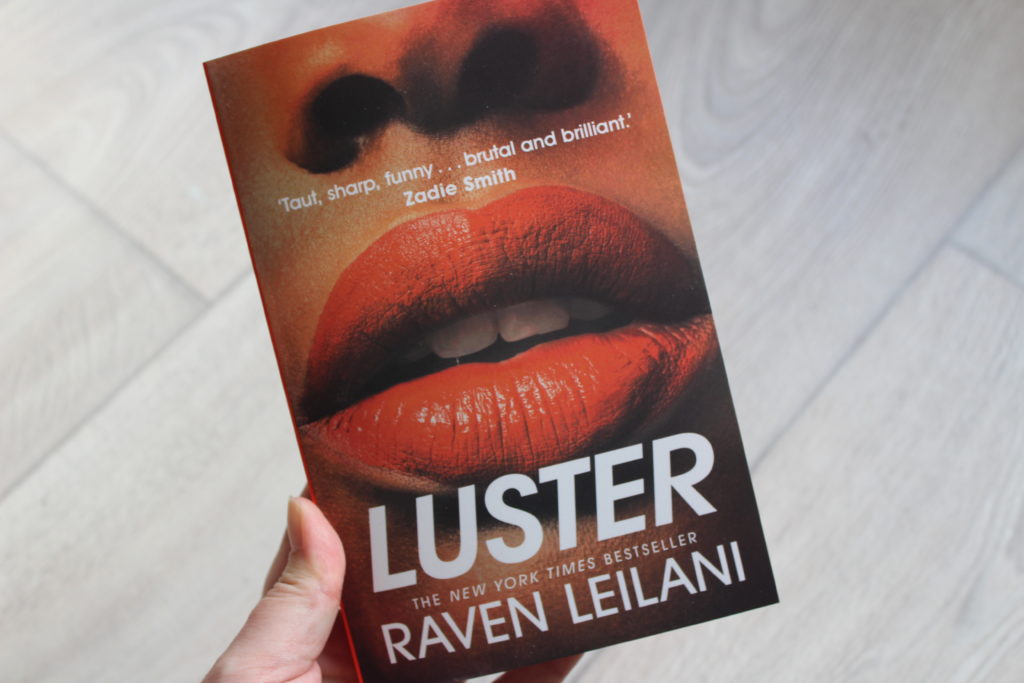 A close up photo of the cover of Luster by Raven Leilani. The image on the cover shows a closeup of a pair of lips.