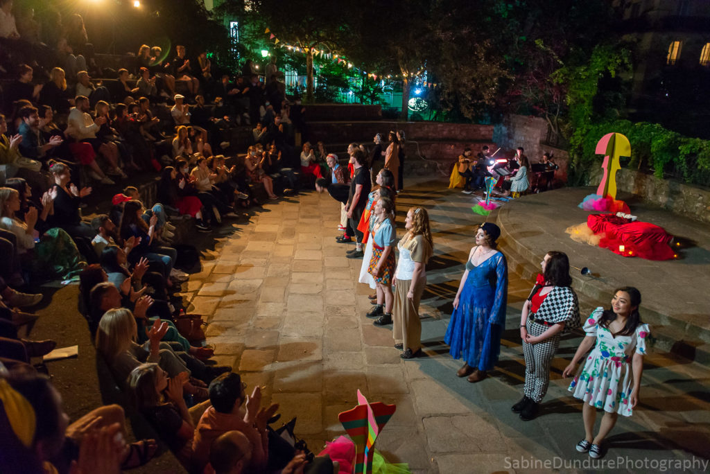 A photo of the curtain call for Romeo and Juliet by Cygnet Theatre. The cast is standing in a line in front of the stage on the right, while the audience is seated on the left.