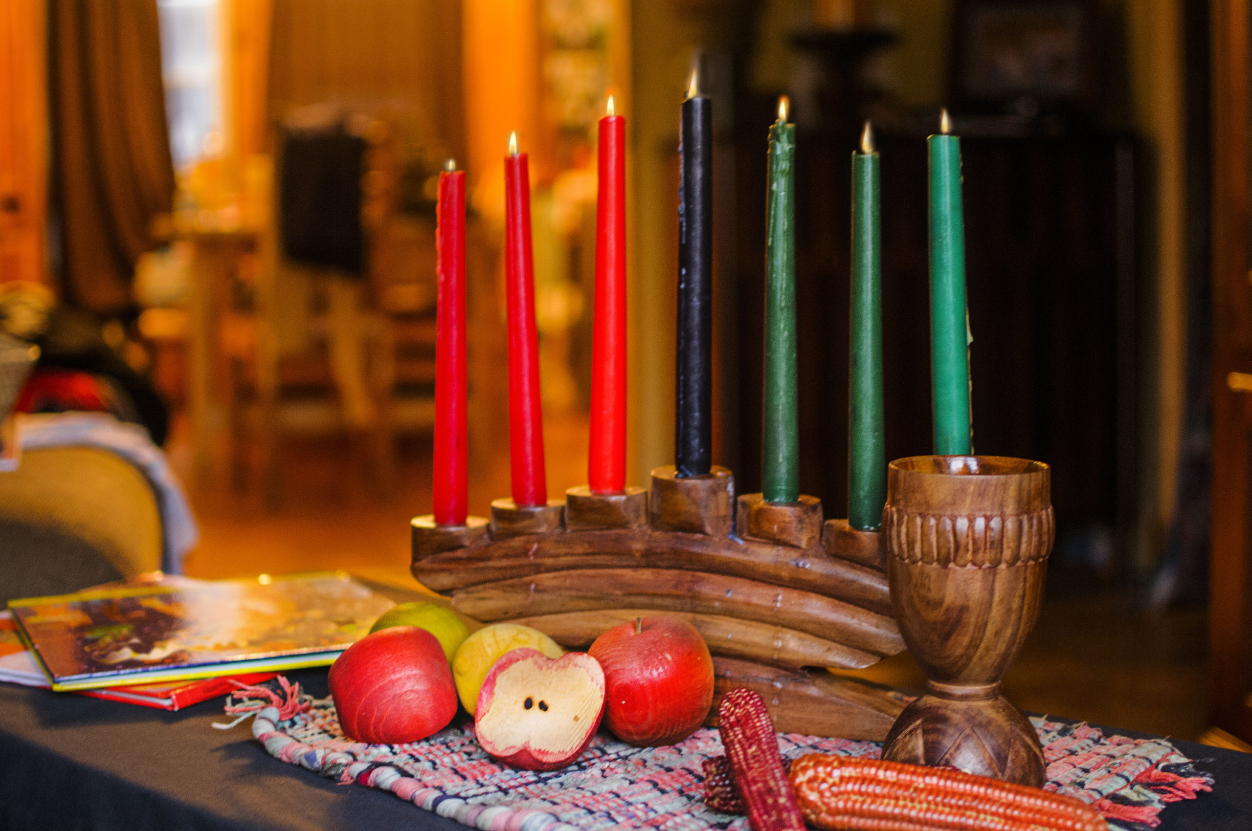 A photo of a table decorated for Kwanzaa. There is a kinara with seven unlit candles, with apples sitting in front.