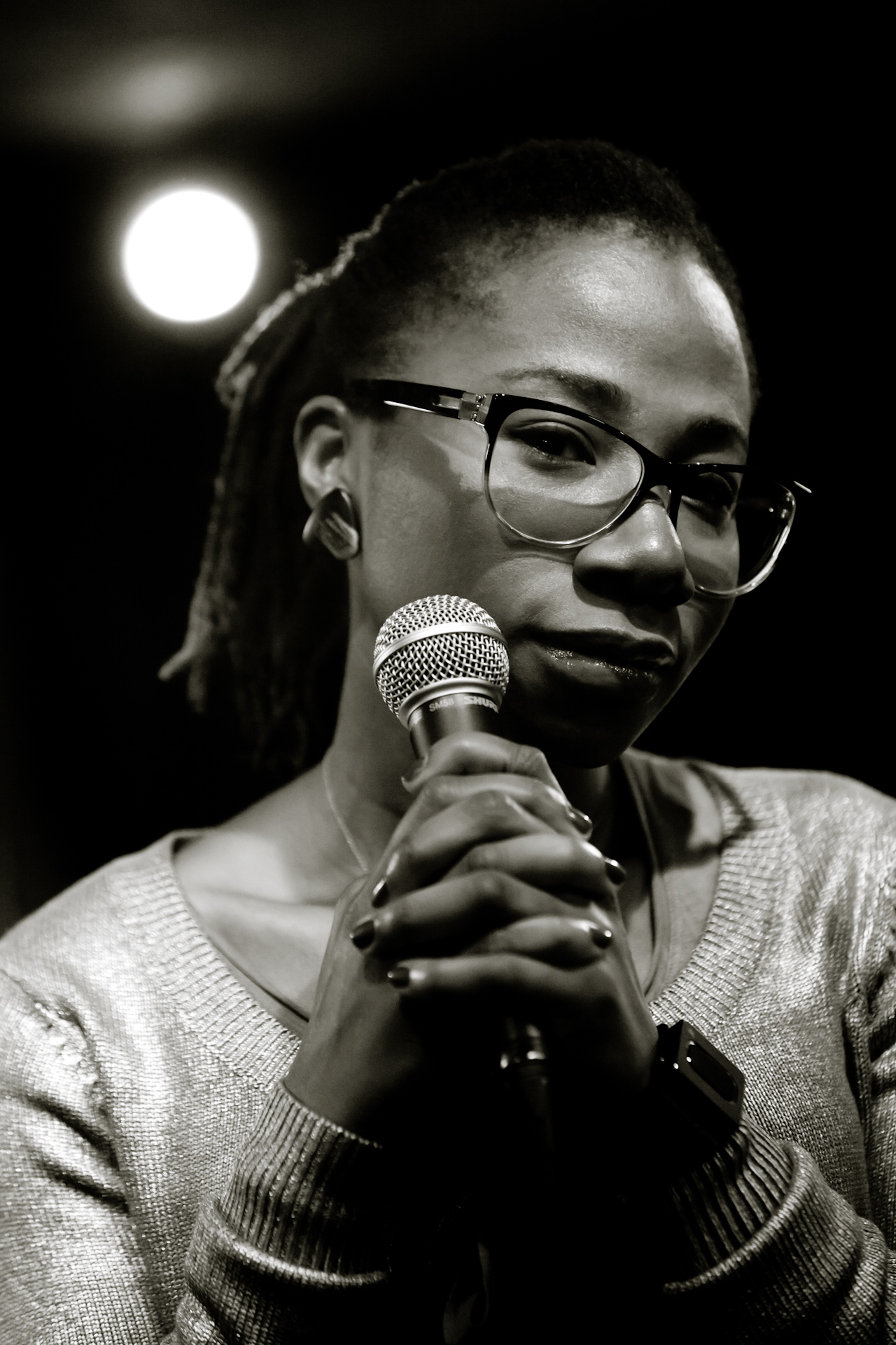A black and white photo of the singer Asa. She is holding a microphone with both hands and looking off camera.