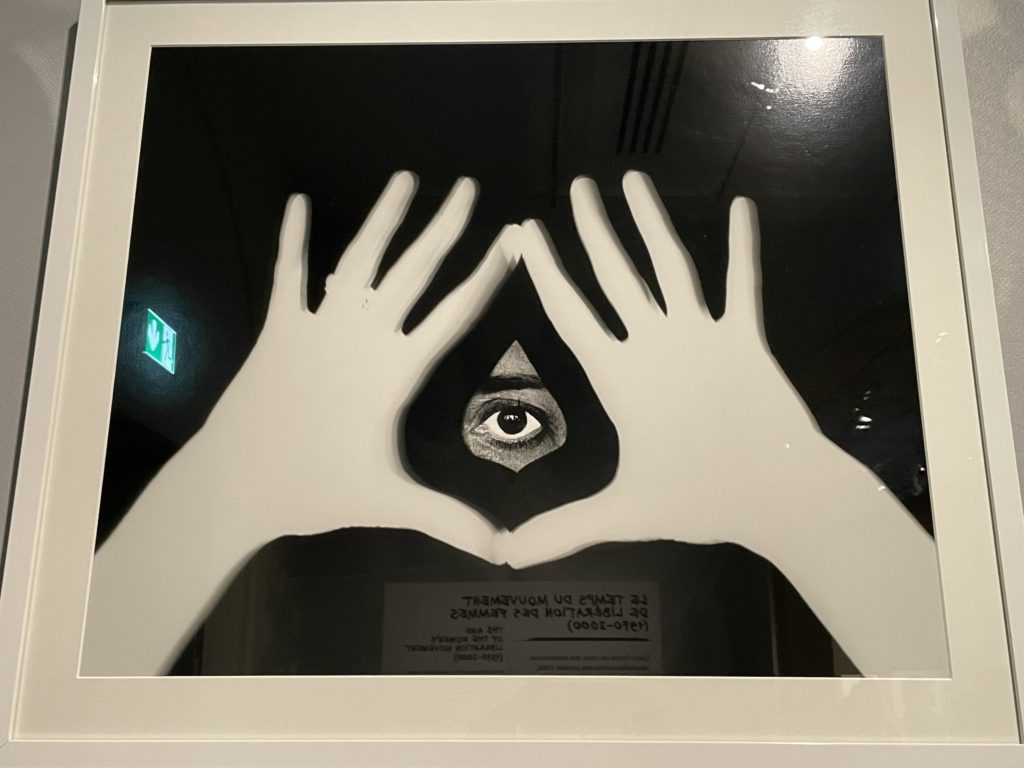 A photo of Feminist Hands #4 by Esther Ferrer. The artwork shows two hands held together, palms facing outwards, the thumbs and forefingers touching. A single eye is looking through the gap made by the thumbs and forefingers.
