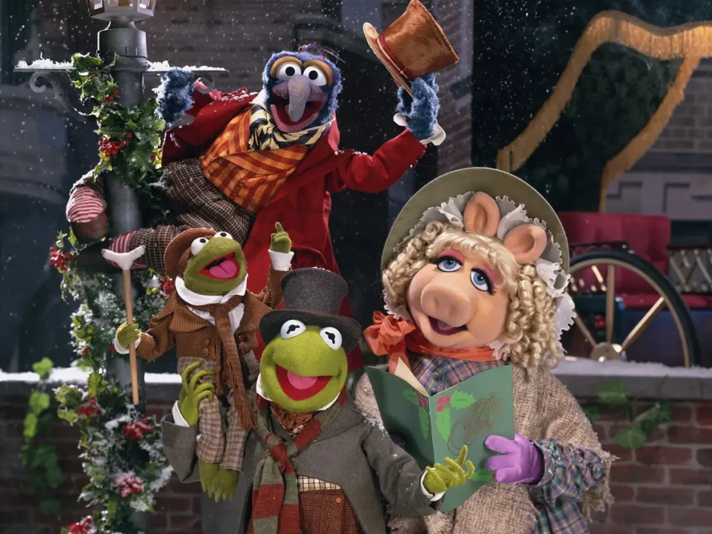 A marketing image from The Muppet Christmas Carol. The photo is of Kermit, Miss Piggy, Gonzo, and Tiny Tim, all dressed in Victorian costumes, posing on a street in London.