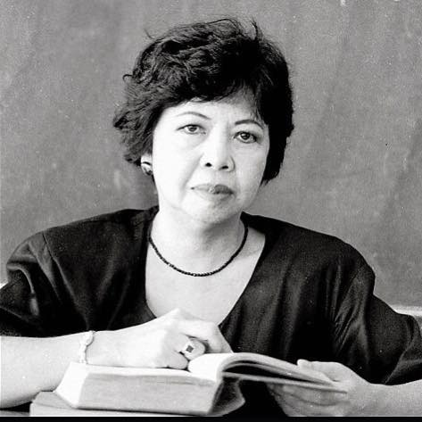 A black and white headshot of Ophelia Dimalanta. She is holding a book and looking straight into the camera.