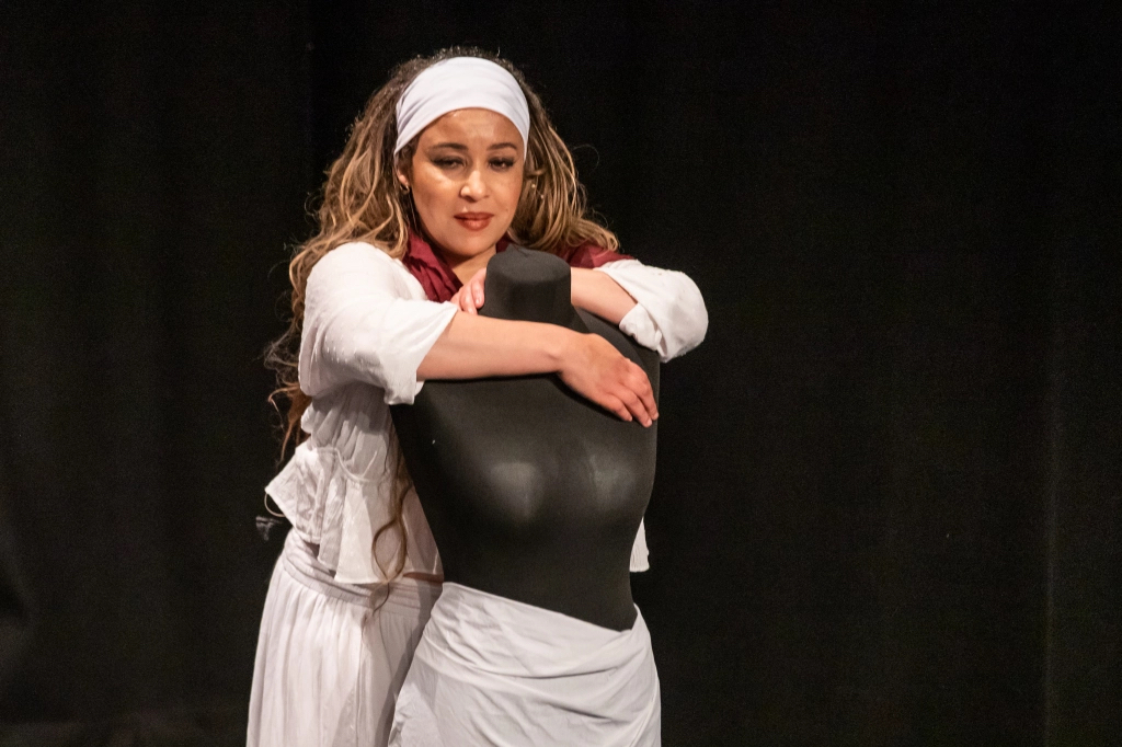 A photo of Catherine Bisset onstage during a scene from Placeholder. She is standing with her arms around a headless mannequin.