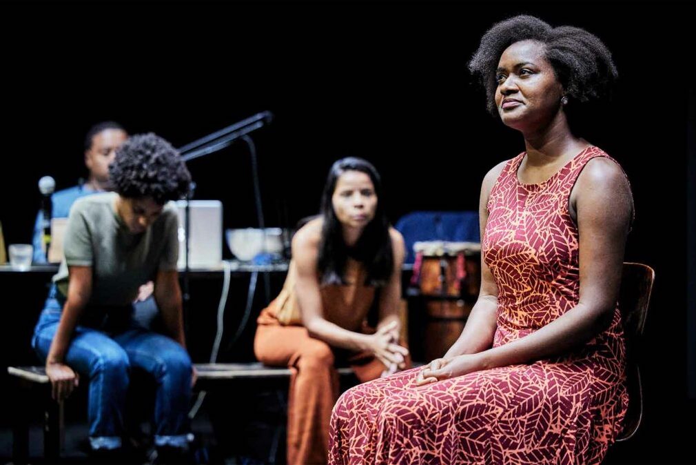 A production still from Depois do Silencio. Four performers are seated onstage in costume.