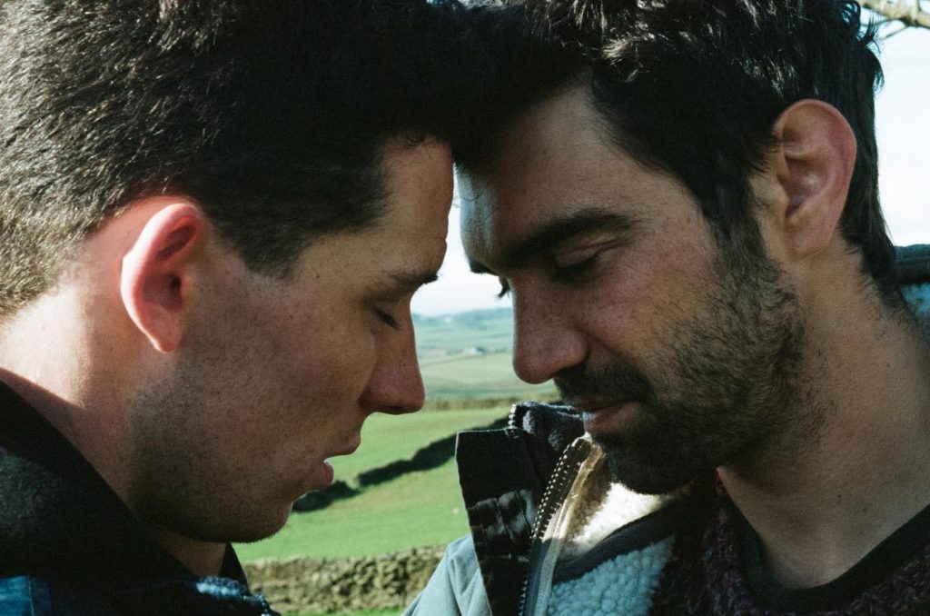 A photo still from God's Own Country. It is an extreme close up of the two lead actors leaning into each other, foreheads touching and eyes closed.